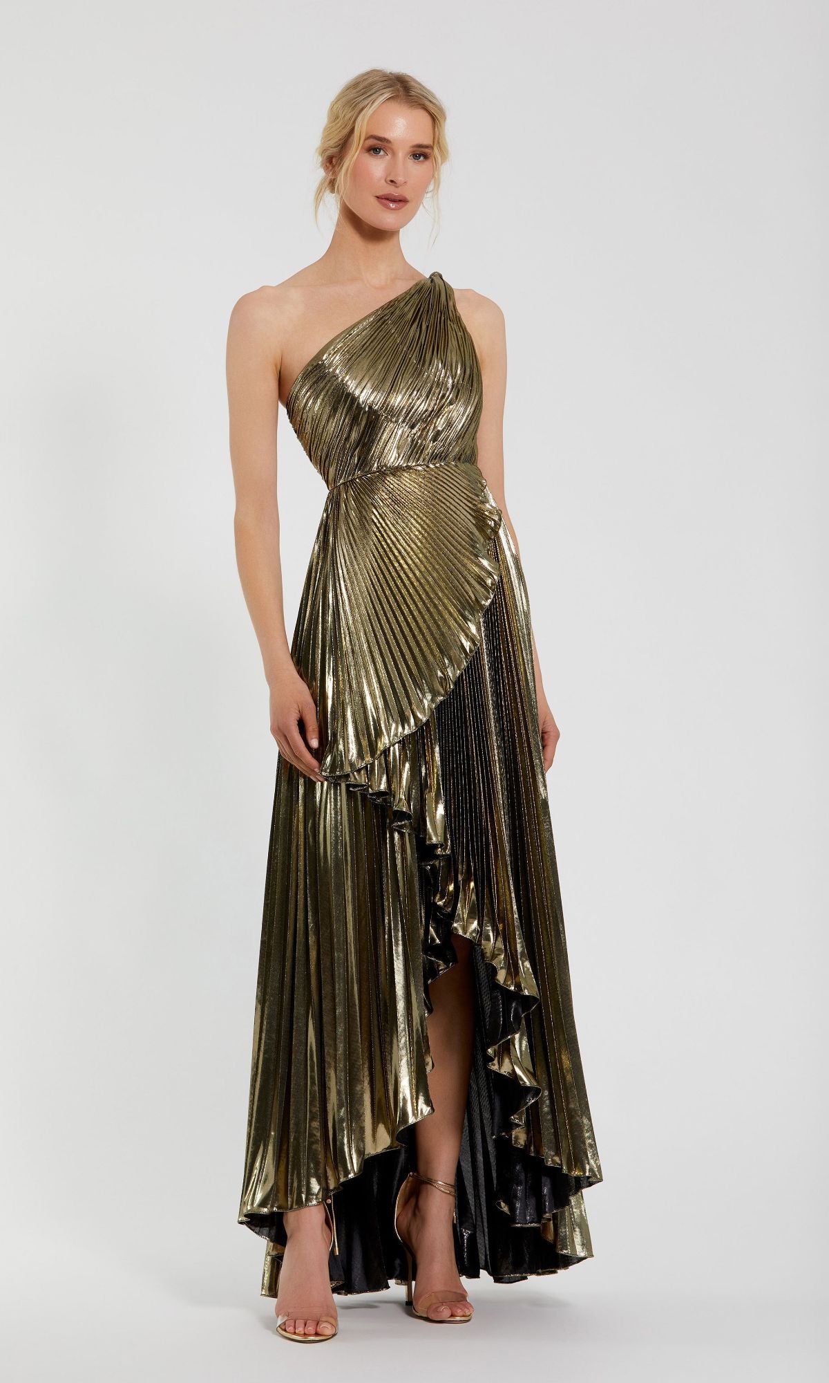 A woman models the Mac Duggal 49910 Gold Pleated Prom Dress with a one-shoulder design, metallic pleated fabric, asymmetrical hem, and ruffled detailing against a plain white background.